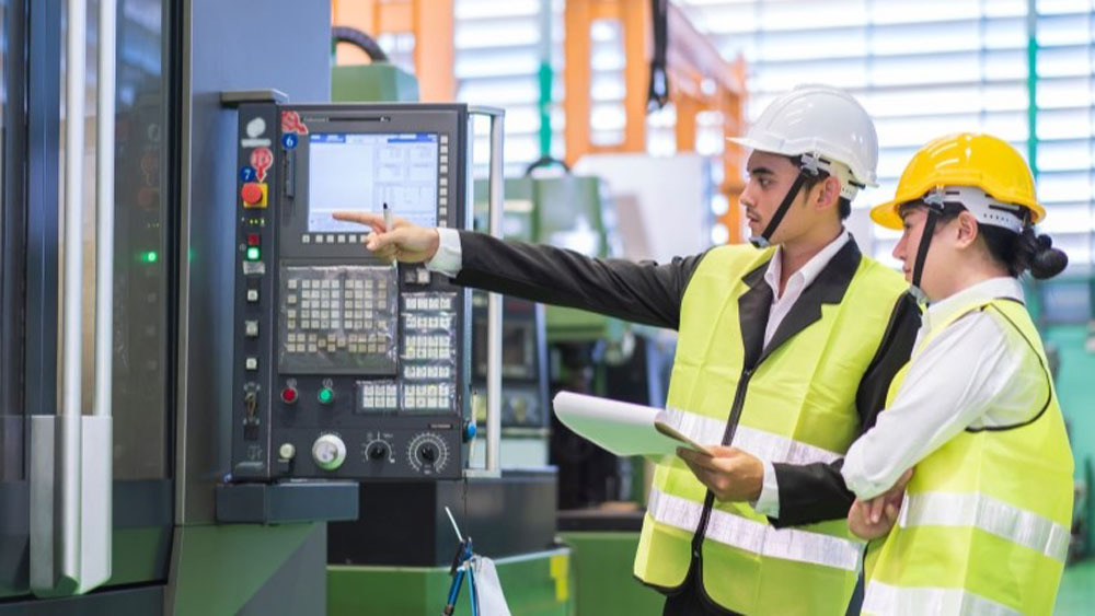 Two workers in neon yellow vests pointing at a screen