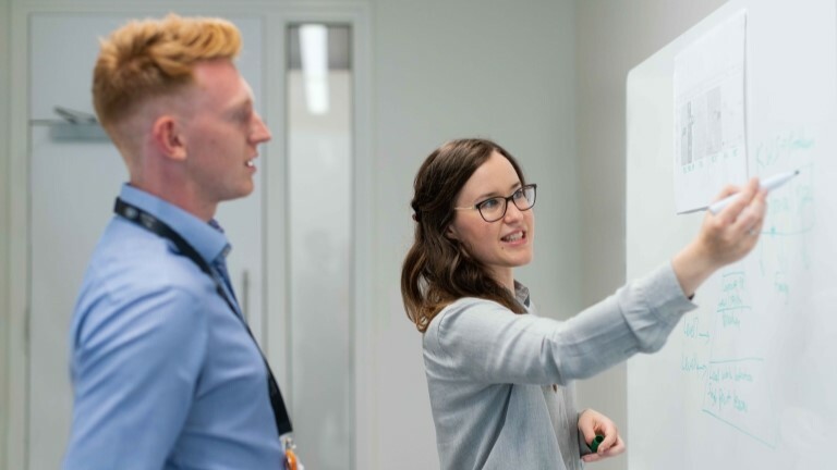 Two workers pointing at a whiteboard