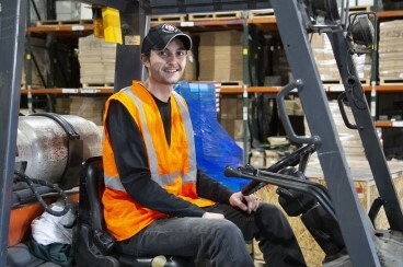 A man in a neon orange vest driving a forklift